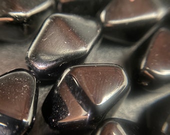 Op de afbeelding: Een close-up van een groep zwarte getrommelde stenen. De stenen zijn glad en glanzend, met een licht reflecterend oppervlak.