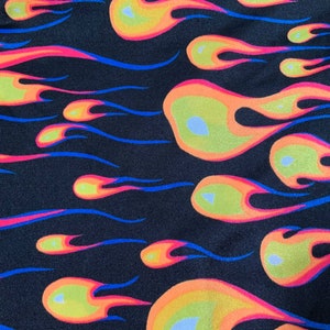 May include: A black fabric with a repeating pattern of orange, yellow, and pink flames. The flames are outlined in blue.