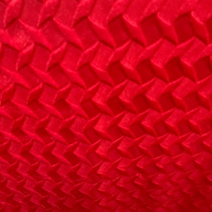 May include: Red fabric with a textured, geometric pattern of raised squares.