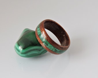 May include: A wooden ring with a green malachite inlay. The ring is next to a piece of malachite.