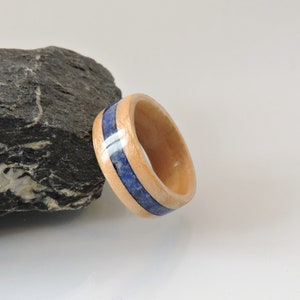 Puede incluir: Un anillo de madera con una incrustación de lapislázuli azul. El anillo está hecho de madera de arce y tiene un acabado natural.