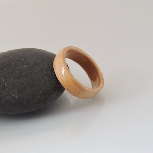 Pode incluir: Um anel de madeira de cor castanho claro com um acabamento liso. O anel é feito de madeira natural e tem um design simples.