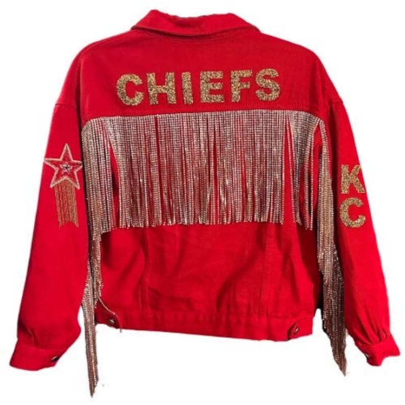 Pode incluir: Casaco de ganga vermelho com letras douradas brilhantes "CHIEFS" nas costas. O casaco apresenta franjas douradas e uma estrela na manga esquerda. "KC" est&aacute; escrito em glitter dourado na manga direita.