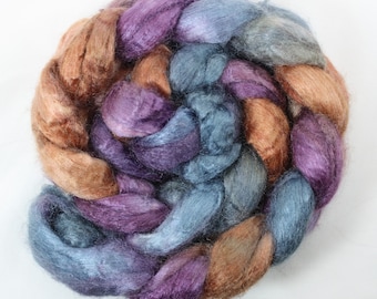 May include: A bundle of hand-dyed silk fiber in shades of brown, purple, and blue. The fiber is arranged in a loose braid.