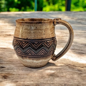 May include: A brown ceramic mug with a geometric pattern around the middle. The mug has a rounded body and a handle.