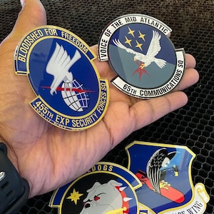 May include: Four blue and gold military unit patches with different designs. The patches feature a white eagle, a bulldog, a falcon, and a globe. The patches are on a black honeycomb background.