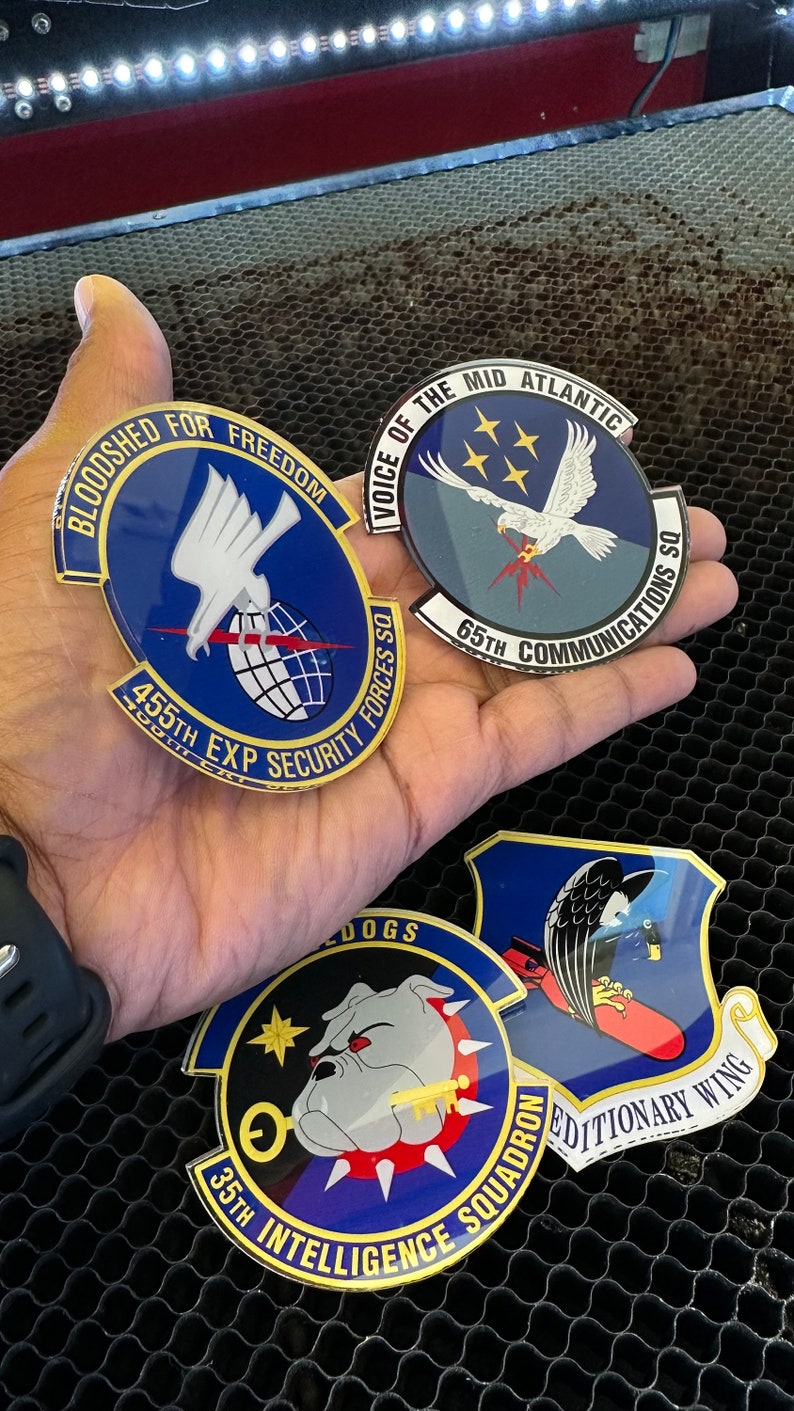 May include: Four blue and gold military unit patches with different designs. The patches feature a white eagle, a bulldog, a falcon, and a globe. The patches are on a black honeycomb background.