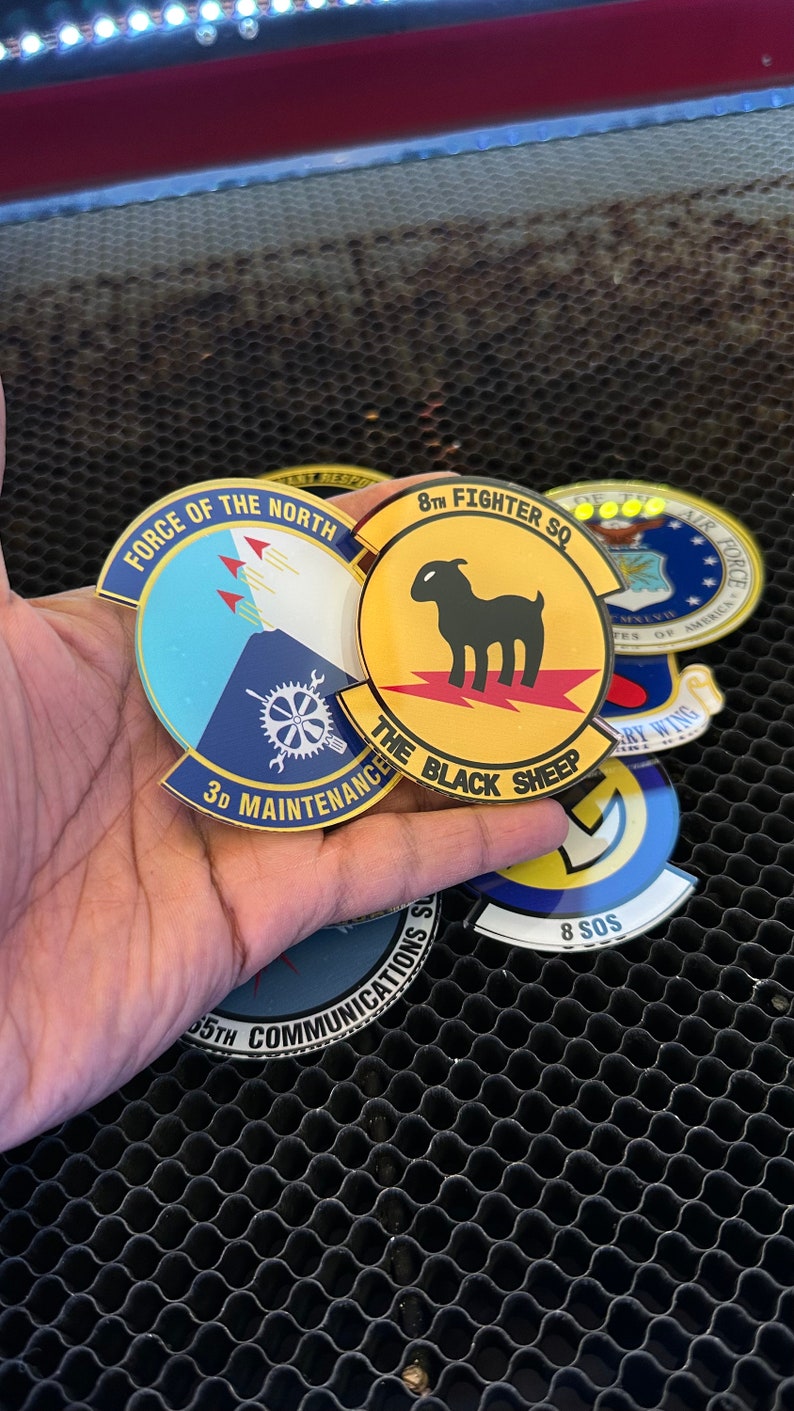 May include: A collection of five round, gold-colored patches with various designs and text. The patches feature a blue and white patch with the text "Force of the North" and "3D Maintenance", a yellow patch with the text "8th Fighter SQ" and "The Black Sheep", a blue and white patch with the text "65th Communications", a yellow patch with the text "8 SOS", and a blue and white patch with the text "US Air Force" and "United States of America".