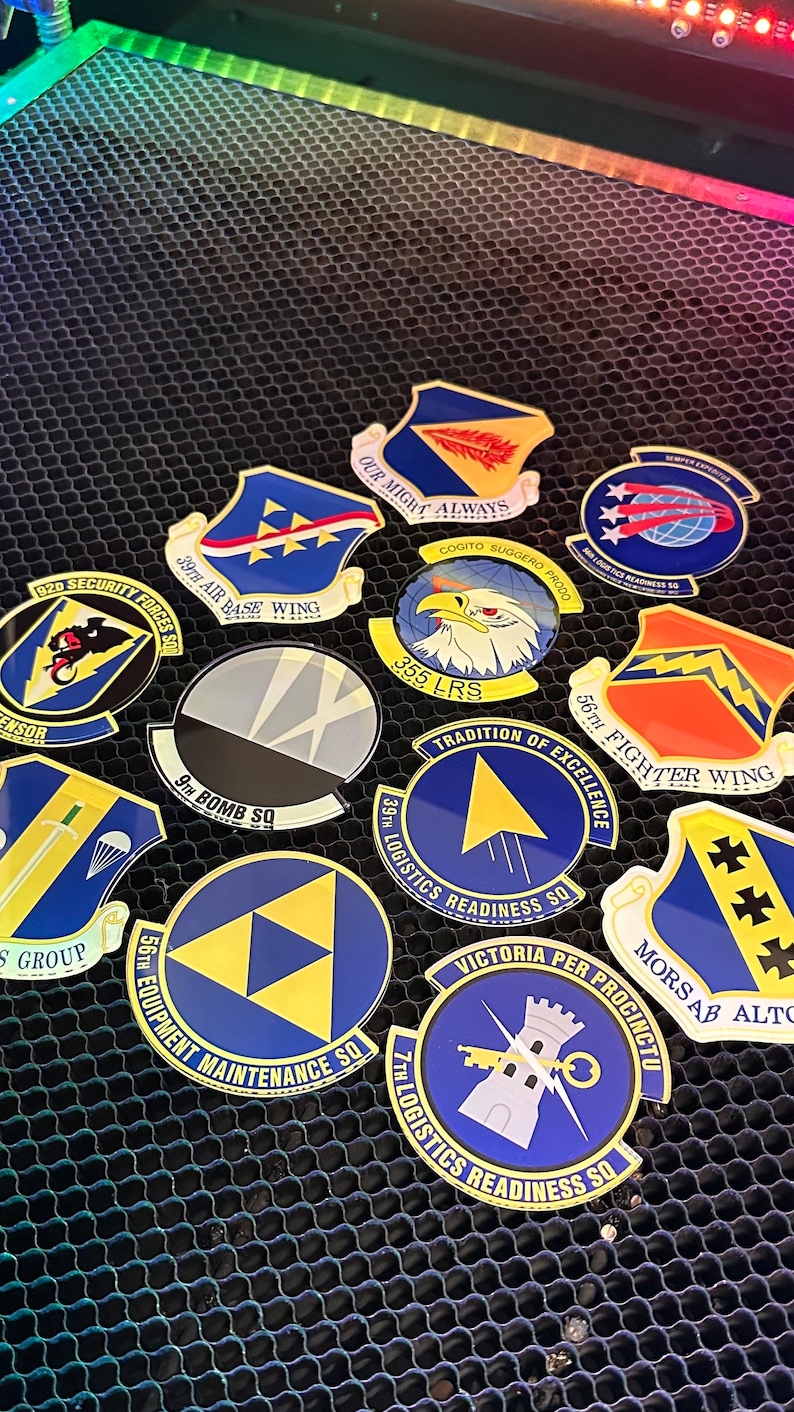 May include: A collection of ten round, blue and gold military unit patches with various designs and text. The patches are arranged on a black honeycomb surface.