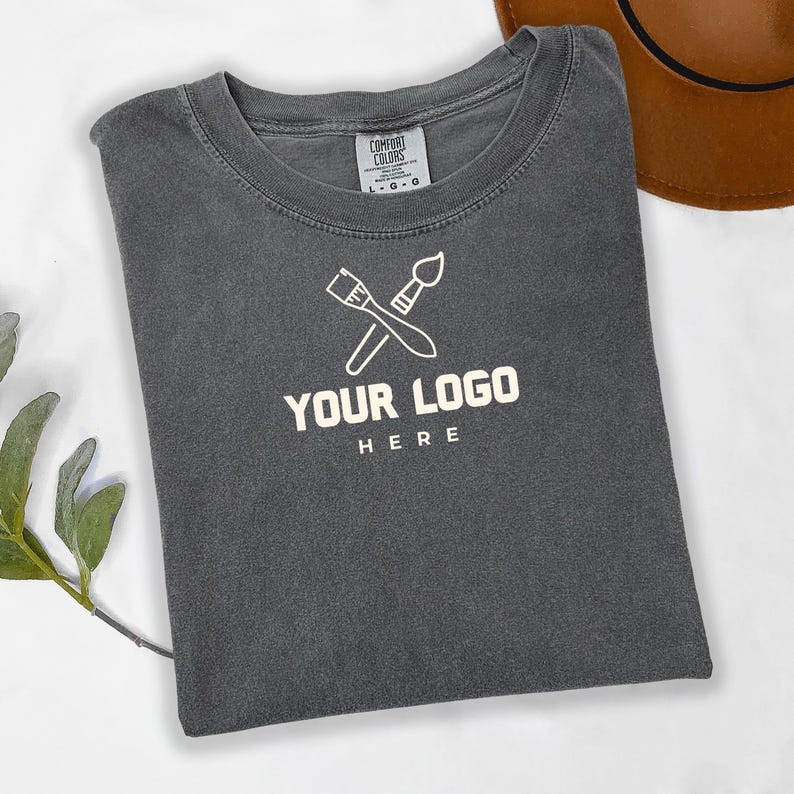 May include: A dark gray t-shirt with a white paintbrush and palette knife logo. The logo says "YOUR LOGO HERE".