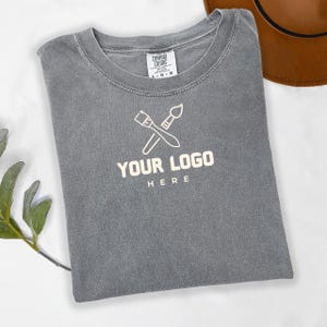 May include: Gray t-shirt with a white paintbrush and palette logo and the text "YOUR LOGO HERE".