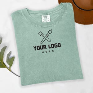 May include: A light green t-shirt with a paintbrush and palette logo and the text "YOUR LOGO HERE".