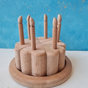 May include: A wooden toy birthday cake with six candles. The cake is made of five separate pieces that fit together. The candles are removable.