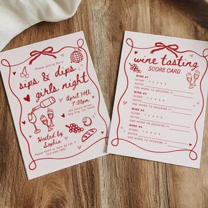 May include: Two pink cards with red illustrations and text. One card reads "sips & dips girls night" with event details. The other is a wine tasting score card. Both cards are on a wooden tray.