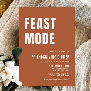 Puede incluir: Una tarjeta de invitación marrón con texto blanco que dice "FEAST MODE" e invita a los invitados a una cena de Friendsgiving el 21 de noviembre a las 3 pm. La tarjeta incluye la dirección y la información de RSVP.