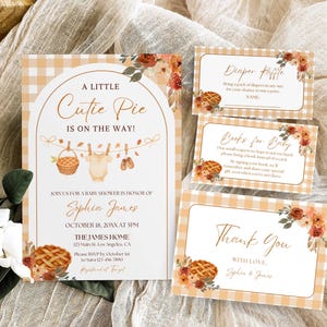 May include: Baby shower invitation set with a rustic theme. The main invitation features the text "A Little Cutie Pie Is On The Way!" with a basket, baby clothes, and shoes illustration. Includes diaper raffle, books for baby, and thank you cards.