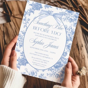 Op de afbeelding: Een witte uitnodiging met blauwe bloemenmotieven en een blauw lint. De tekst luidt "Something Blue Before I Do". De uitnodiging is voor een bruidsdouche voor Sophia James op 23 september om 14:30 uur in het James Hotel.
