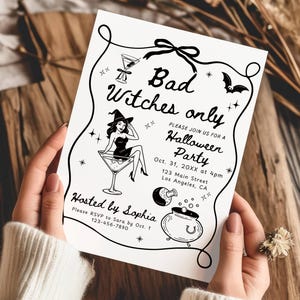 以下が含まれることがあります： 「Bad Witches only」のテキストが入った白黒のハロウィーンパーティーの招待状。マティーニグラスの中の魔女、コウモリ、大釜のイラストが特徴です。招待状は人が持っています。