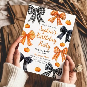 May include: A birthday party invitation with orange and black bows and pumpkins. The invitation reads "Sophia's Birthday Party" with the date, time, and location. The invitation is held by a person wearing a white sweater.