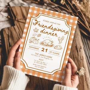 May include: An invitation for a Friendsgiving dinner, held on November 21st at 4:00 PM. The design features a gingham pattern and illustrations of pumpkins, a turkey, and other festive elements. The invitation is held by a person.