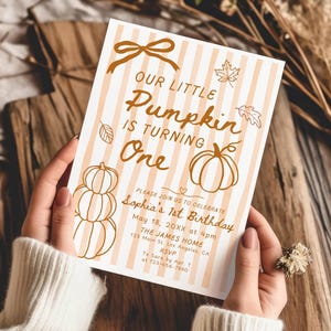 Puede incluir: Una invitación de cumpleaños con temática de calabaza. La tarjeta tiene un fondo a rayas verticales en crema y melocotón. El texto "Our Little Pumpkin is Turning One" se muestra con ilustraciones de calabazas y hojas. La invitación incluye la fecha, hora y lugar.