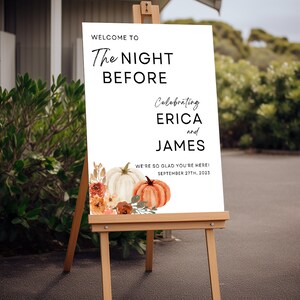 May include: White sign with black text announcing "The Night Before" celebrating Erica and James. The sign is decorated with a watercolor illustration of pumpkins and flowers. The date September 27th, 2023 is also included.