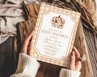 May include: A rectangular baby shower invitation card featuring a light orange and white gingham border. The center displays a brown pumpkin illustration with leaves and acorns, followed by text detailing an event for Sophia James.