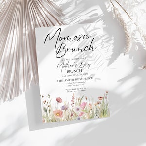 Op de afbeelding: Een witte uitnodigingskaart met zwarte tekst die een Moederdagbrunch aankondigt. De tekst luidt "Momosa Brunch" en "U bent uitgenodigd voor een Moederdagbrunch". De uitnodiging bevat de datum, tijd en locatie van de brunch. De kaart is versierd met een aquarel-illustratie van roze en paarse wilde bloemen.