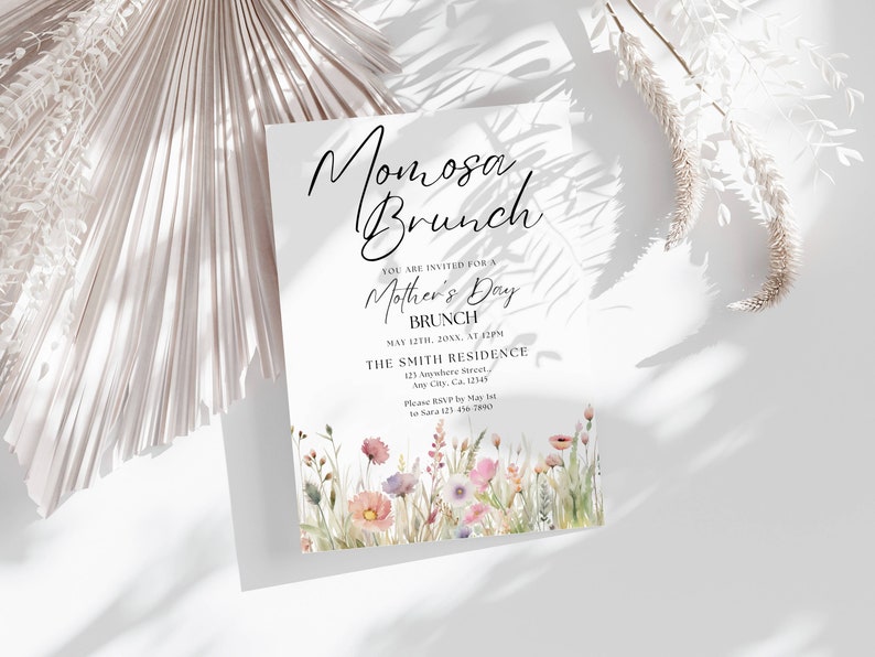 Op de afbeelding: Een witte uitnodigingskaart met zwarte tekst die een Moederdagbrunch aankondigt. De tekst luidt "Momosa Brunch" en "U bent uitgenodigd voor een Moederdagbrunch". De uitnodiging bevat de datum, tijd en locatie van de brunch. De kaart is versierd met een aquarel-illustratie van roze en paarse wilde bloemen.