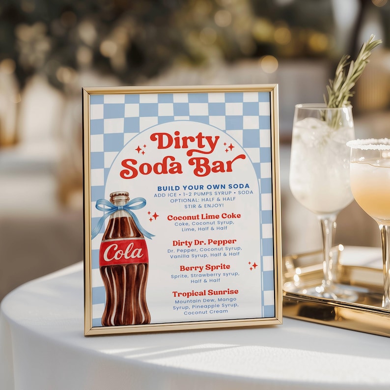 May include: A framed sign with a gold border, featuring a "Dirty Soda Bar" design. The sign includes a Coca-Cola bottle illustration and a menu with soda recipes like Coconut Lime Coke and Berry Sprite. The background has a blue and white checkered pattern.