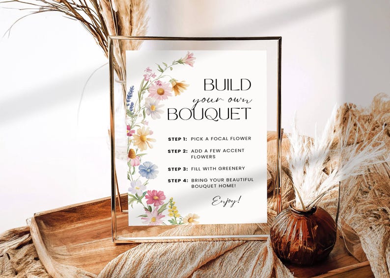 May include: A gold-framed sign with the text "Build Your Own Bouquet" and instructions, decorated with watercolour flowers. The sign is on a wooden tray with dried plants and a vase with dried flowers.