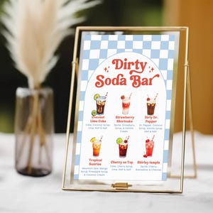 May include: A gold-framed sign with a blue and white checkered background displays a "Dirty Soda Bar" menu. The menu features six colorful soda drink illustrations with their ingredients listed below each drink.