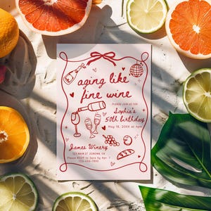 May include: A pink invitation with the text "aging like fine wine" surrounded by illustrations of wine bottles, glasses, and grapes. The invitation is surrounded by sliced citrus fruits, strawberries, and a green leaf.