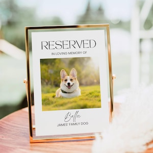 Puede incluir: Un cartel con marco dorado con el texto "RESERVED" en memoria de Bella, la perra de la familia James. Una foto de un perro corgi está en el centro del cartel.
