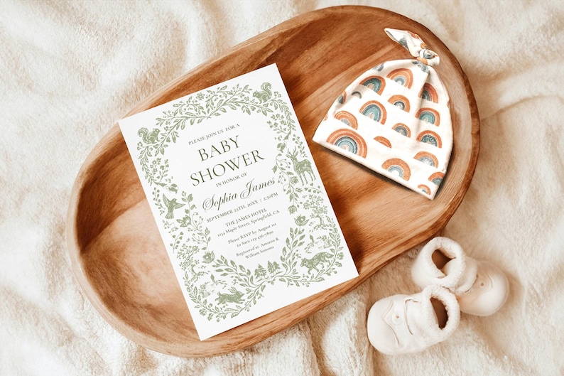 May include: A wooden tray holds a baby shower invitation, a rainbow-patterned hat, and white baby shoes. The invitation features a floral border and text. The hat has a repeating rainbow design.