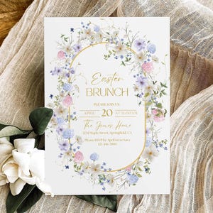 May include: A rectangular white invitation card featuring a gold oval frame surrounded by a watercolor floral wreath of pink, blue, and white flowers. The text reads Easter Brunch, Please Join Us, April 20 at 11:00 AM, The Jones Home, 1234 Maple Street, Springfield, CA, Please RSVP by April 1st to Sara 123-456-7890.