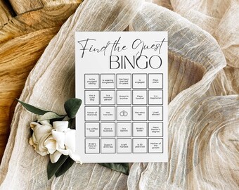 Può includere: Una scheda di gioco Find the Guest Bingo bianca con testo nero e una griglia di venticinque quadrati contenenti vari suggerimenti e un'icona di anelli. La scheda presenta una combinazione di caratteri script e sans-serif su carta.