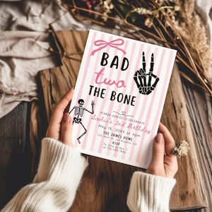 May include: A rectangular birthday invitation card featuring a pink and white vertical striped background. The text reads BAD two THE BONE with a skeleton hand making a peace sign, a small skeleton, and event details for Sophia's 2nd Birthday.