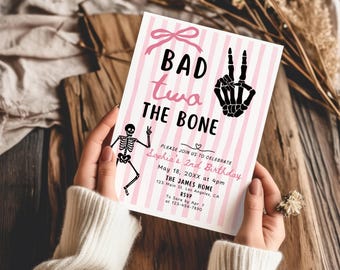 May include: A rectangular birthday invitation card featuring a pink and white vertical striped background. The text reads BAD two THE BONE with a skeleton hand making a peace sign, a small skeleton, and event details for Sophia's 2nd Birthday.