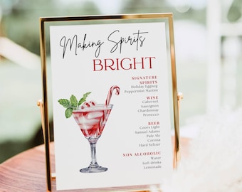 Op de afbeelding: Een gouden lijst met de tekst "Making Spirits Bright" en een lijst met alcoholische en niet-alcoholische dranken. Het bord heeft een aquarel-illustratie van een martini-glas met een snoepstok en rode en witte pepermunt.