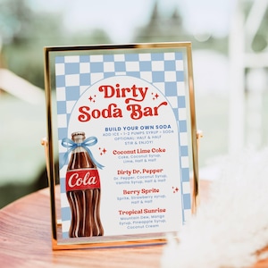 Pode incluir: Um letreiro emoldurado com uma borda dourada, apresentando um design retrô para um "Dirty Soda Bar". O letreiro inclui uma ilustração de uma garrafa de Coca-Cola e uma lista de receitas de refrigerantes como Coconut Lime Coke e Berry Sprite. O fundo tem um padrão xadrez azul e branco.