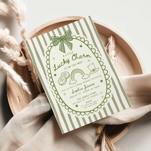 May include: A St. Patrick's Day baby shower invitation with a green and white striped background. The invitation features a green bow, shamrocks, a rainbow, and the text "A Little Lucky Charm Is On The Way."