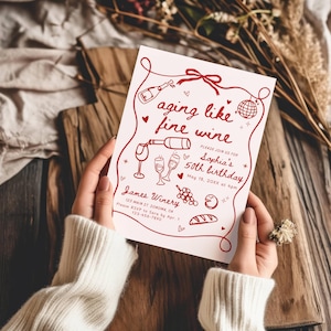 May include: A white invitation card with red text and illustrations, held by a person. The card reads "aging like fine wine" and announces Sophia's 50th birthday. Includes wine-themed graphics and the James Winery address.