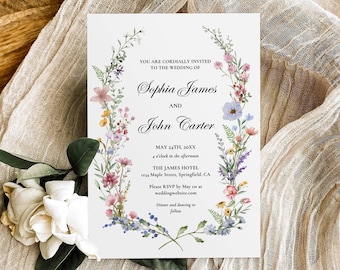 May include: A white wedding invitation card featuring a floral wreath border with pink, blue, and yellow wildflowers. The text reads: You are cordially invited to the wedding of Sophia James and John Carter, May 24th, 20XX, 4 o'clock in the afternoon, The James Hotel, 1234 Maple Street, Springfield, CA. Please RSVP by May xx at weddingwebsite.com. Dinner and dancing to follow.