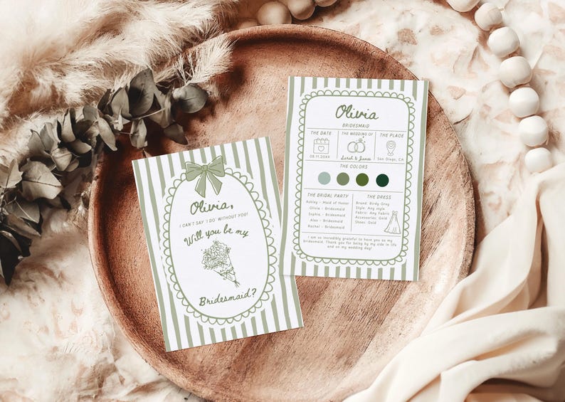 May include: Two invitation cards with a green and white striped design. The cards feature the name "Olivia" and the text "Will you be my Bridesmaid?" The cards are on a wooden tray with decorative elements.