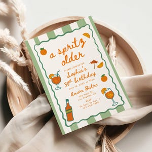 Op de afbeelding: Een rechthoekige uitnodiging met een groen-witte gestreepte rand, met de tekst "a spritz older" en details voor een 30e verjaardag. Oranje illustraties van cocktails en fruit versieren de kaart.