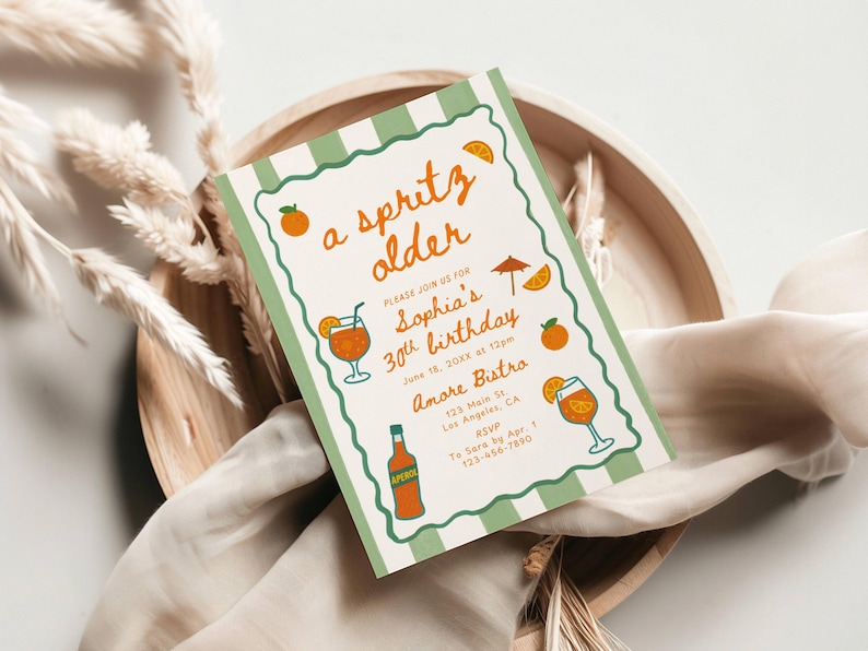 Op de afbeelding: Een rechthoekige uitnodiging met een groen-witte gestreepte rand, met de tekst "a spritz older" en details voor een 30e verjaardag. Oranje illustraties van cocktails en fruit versieren de kaart.