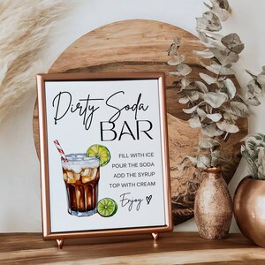 May include: A printable sign with a copper frame that says "Dirty Soda Bar" with a graphic of a glass of soda with ice, lime, and a straw. The sign also includes instructions for making a dirty soda: "Fill with ice, pour the soda, add the syrup, top with cream, Enjoy."