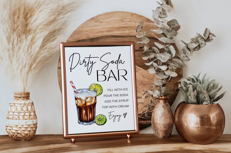 May include: A printable sign with a copper frame that says "Dirty Soda Bar" with a graphic of a glass of soda with ice, lime, and a straw. The sign also includes instructions for making a dirty soda: "Fill with ice, pour the soda, add the syrup, top with cream, Enjoy."