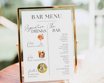 May include: A vertical rectangular bar menu sign in a gold metal frame. The white sign features black text listing wine, beer, spirits, and non-alcoholic drinks. It includes illustrations of an Aperol Spritz, an Old Fashioned, and a photo of a dog.